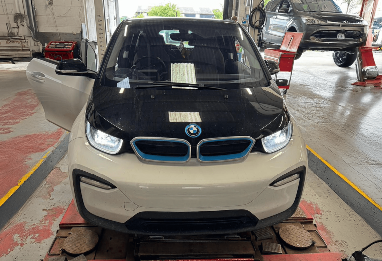 A black and white BMW i series in a bay at Castle Garage EV in Ashby. the car is electric and so has blue around its badge and its grille. The driver side door is open.